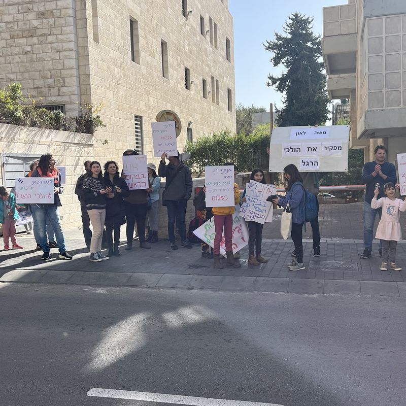 תושבים, הורים וילדים עומדים על המדרכה עם שלטי מחאה למען הולכי הרגל